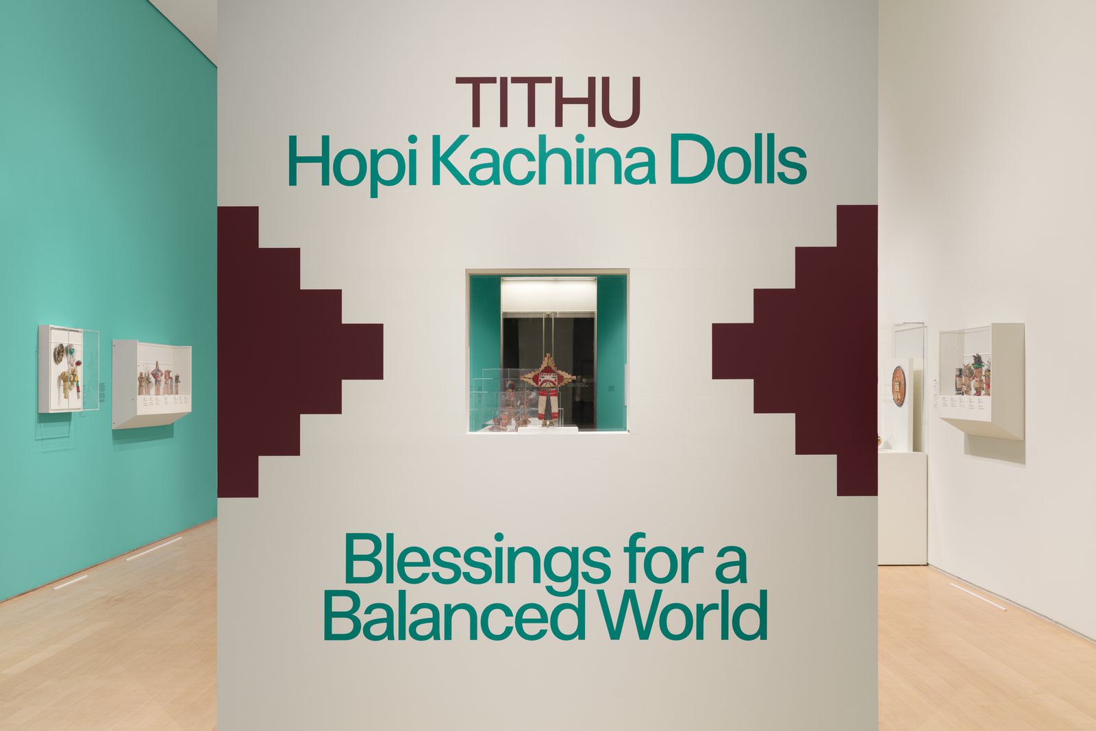 Title wall of “Hopi Kachina Dolls: Blessings for a Balanced World” at the Brooklyn Museum, with a kachina doll in a window between stepped maroon shapes