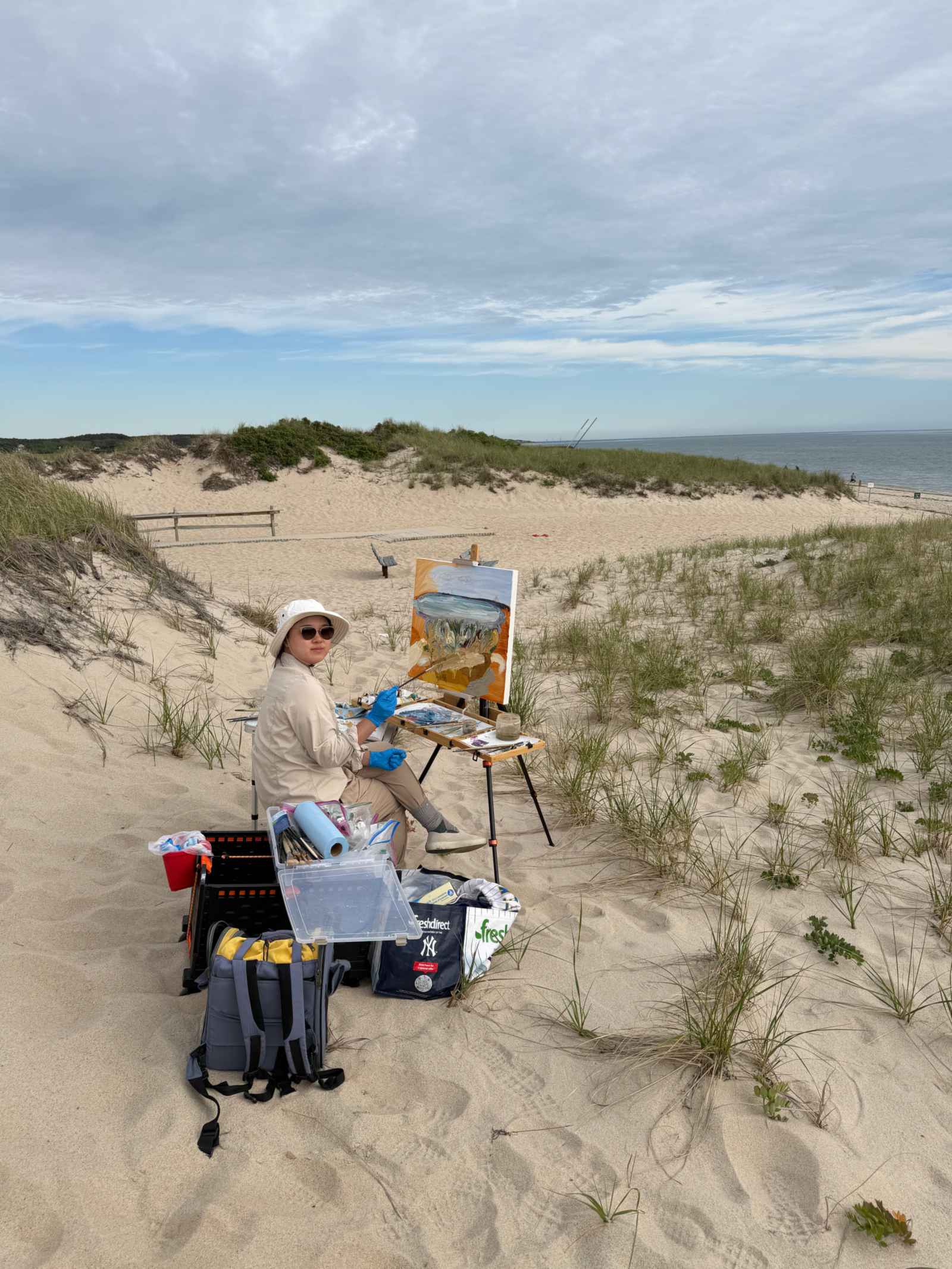 Susan Chen in a sun hat at her easel on a sand dune on Cape Cod
