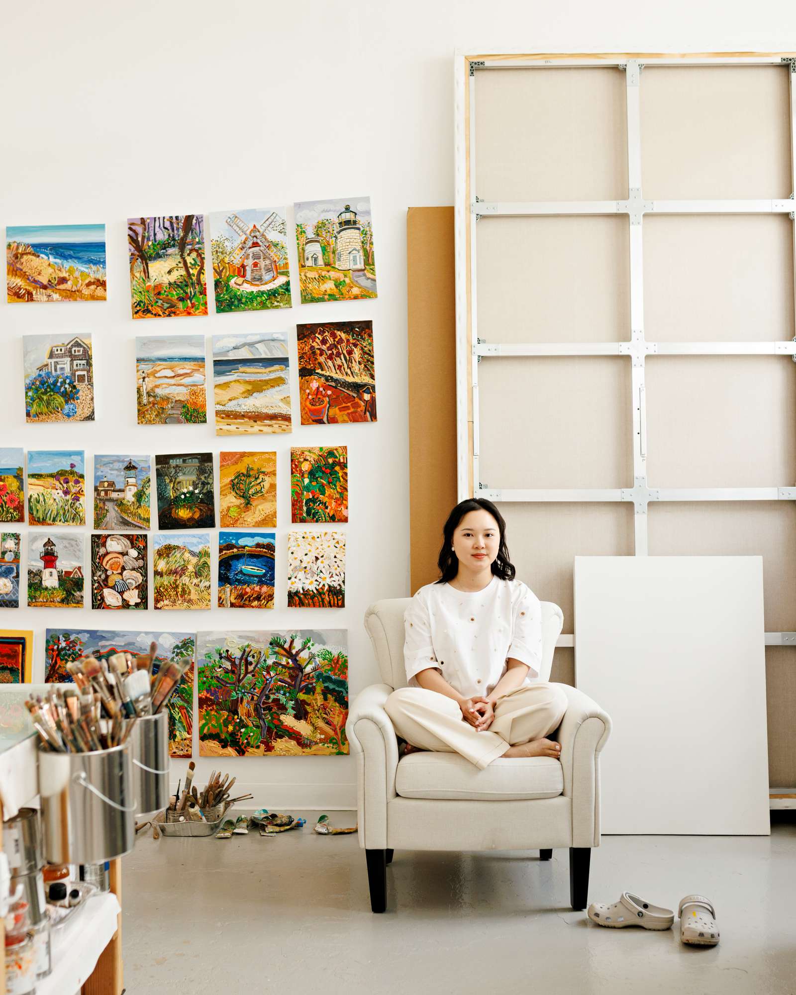 Susan Chen seated in an armchair in her studio, small Cape Cod paintings on the wall behind her