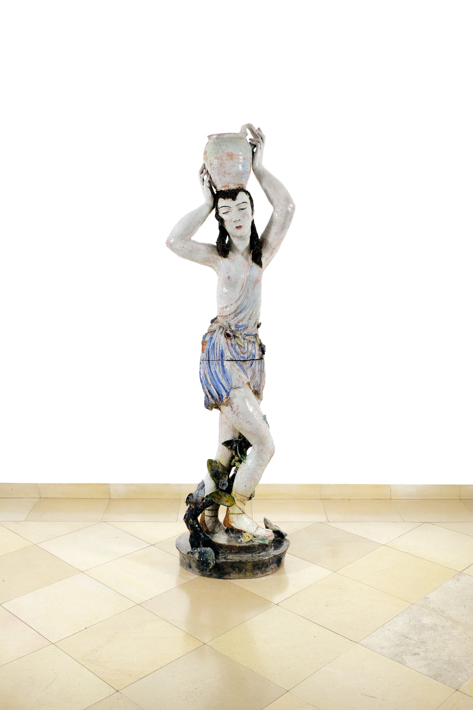 Susi Singer, “Figure with Jug,” a tall glazed ceramic woman in a blue and white patterned skirt holding a jug on her head